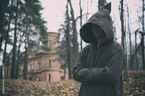 Фотография Mysterious monk or wizard in hooded robe stands in forest against the background of medieval castle or monastery