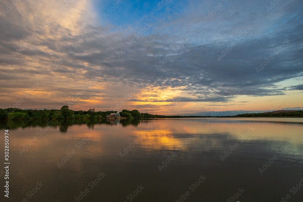 The tranquil waters of Lake Kununurra in the Kimberley region of Western Australia at sunset with tropical thunderstorms in the distance.