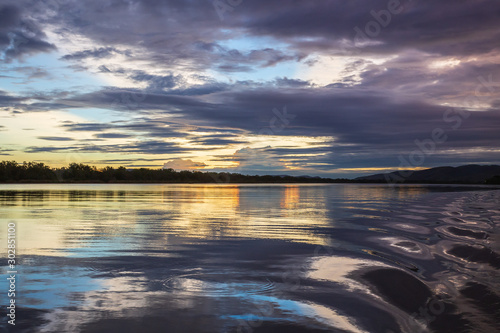 The tranquil waters of Lake Kununurra in the Kimberley region of Western Australia at sunset with tropical thunderstorms in the distance.