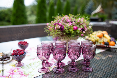 Beautiful glasses of colored purple glass on the table with berries and flowers, composition for catering outdoors