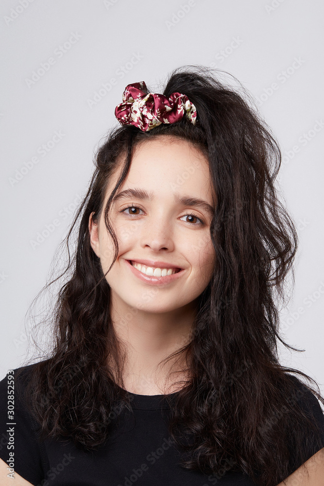 Medium close-up shot of a young brunette European girl with a red satin hair band with a light flower print. The fashion model with dark wavy hair in a half ponytail is wearing a black top Medium close-up shot of a young brunette European girl with a red satin hair band with a light flower print. The fashion model with dark wavy hair in a half ponytail is wearing a black top