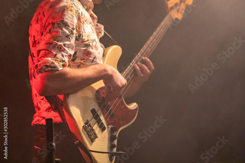 A close up view on electric guitar player viewed from the side as he wearing Shirt with flowers, with smoke and dark in the background