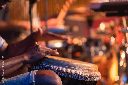 Close-up of man's hands playing on African djembe drum, selective focus on hands with blurry background during a traditional music performance