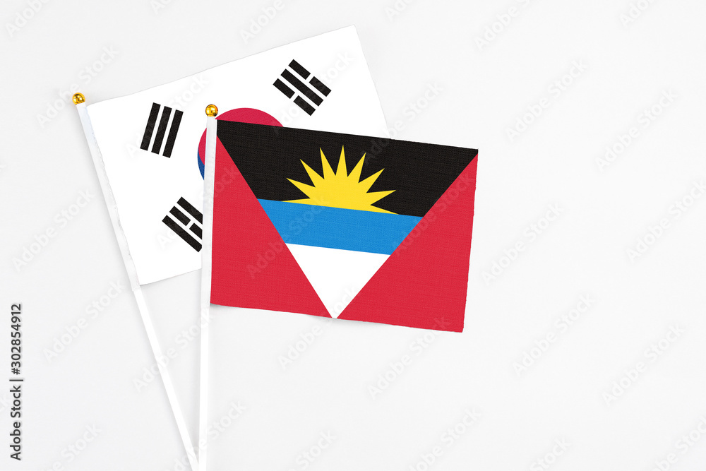 Obraz premium Antigua and Barbuda and South Korea stick flags on white background. High quality fabric, miniature national flag. Peaceful global concept.White floor for copy space.