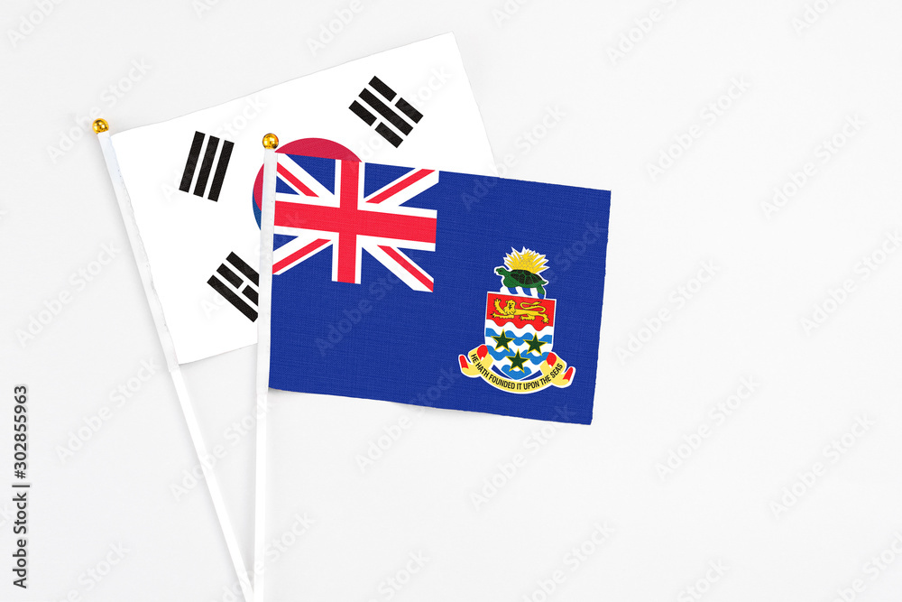 Fototapeta premium Cayman Islands and South Korea stick flags on white background. High quality fabric, miniature national flag. Peaceful global concept.White floor for copy space.