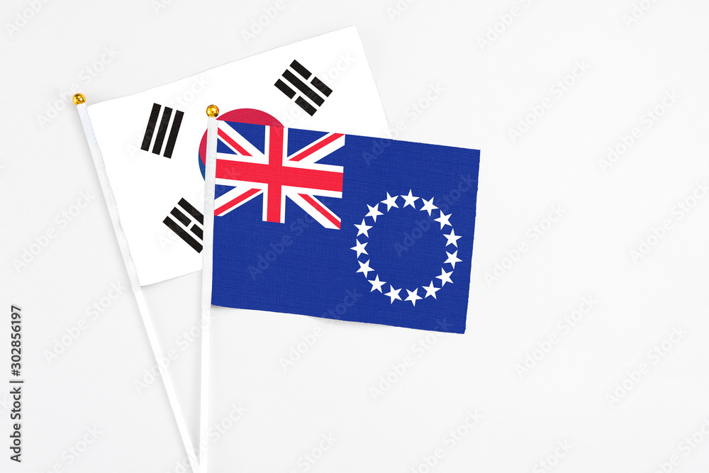 Fototapeta premium Cook Islands and South Korea stick flags on white background. High quality fabric, miniature national flag. Peaceful global concept.White floor for copy space.
