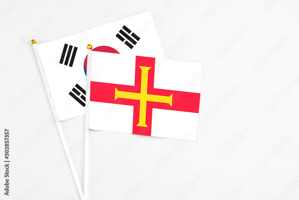 Guernsey and South Korea stick flags on white background. High quality fabric, miniature national flag. Peaceful global concept.White floor for copy space.