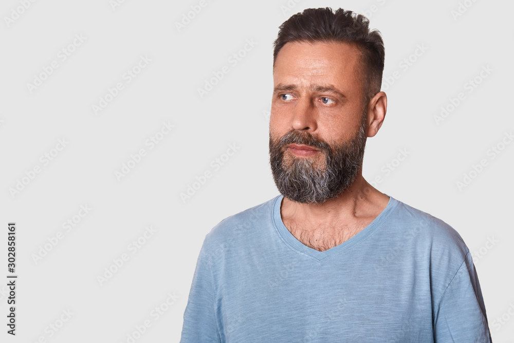 Studio shot of attractive swedish guy with stylish haistyle and beard wearing grey t shirt, looks thoughtful, looking aside thinking about something. Copy space for advertisment or promotion text. Studio shot of attractive swedish guy with stylish haistyle and beard wearing grey t shirt, looks thoughtful, looking aside thinking about something. Copy space for advertisment or promotion text.