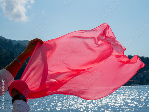 Woman holding a pink scarf that flutters in the wind with the sea in the background