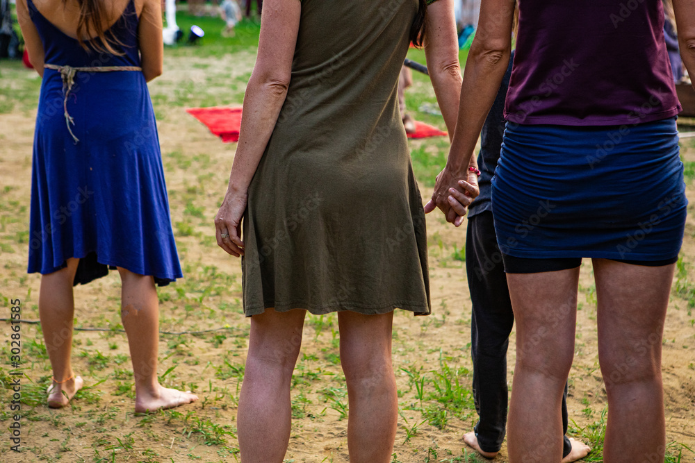 Diverse people enjoy spiritual gathering, close up back view of two women are seen standing and holding each other's hands in nature Diverse people enjoy spiritual gathering, close up back view of two women are seen standing and holding each other's hands in nature