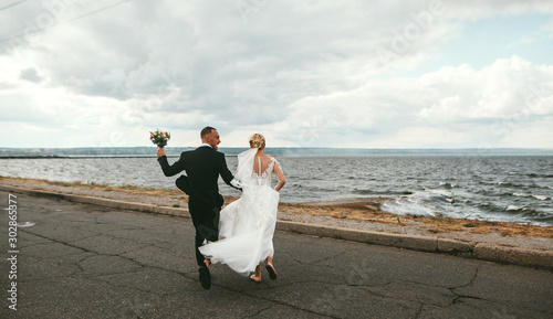 Young wedding beautiful couple, newlyweds running along the beach in honeymoon or wedding day after ceremony