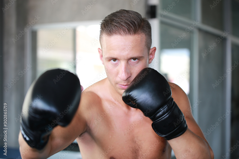 Sportsman muay thai boxer fighting in gloves in boxing cage against fitness gym. Copy Space. Sportsman muay thai boxer fighting in gloves in boxing cage against fitness gym. Copy Space.