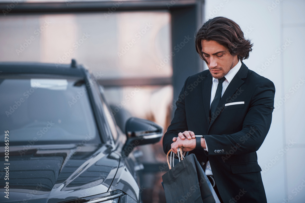 Portrait of handsome young businessman in black suit and tie outdoors near modern car Portrait of handsome young businessman in black suit and tie outdoors near modern car