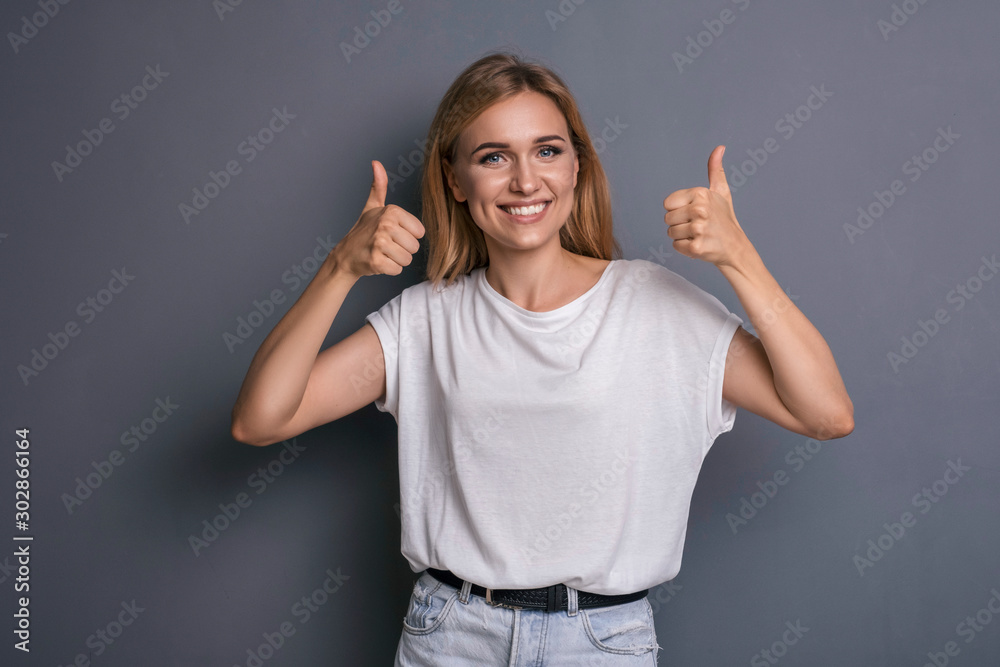 Caucasian woman in neutral casual outfit standing on a neutral grey background. Portrait with emotions: happiness, amazement, joy and satisfaction Caucasian woman in neutral casual outfit standing on a neutral grey background. Portrait with emotions: happiness, amazement, joy and satisfaction