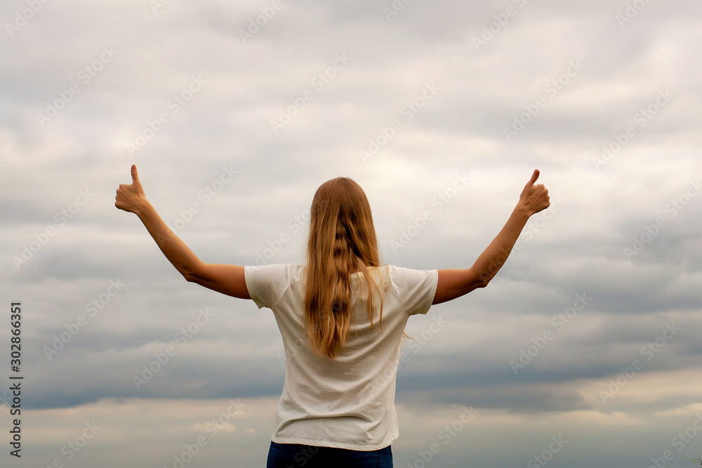 Beautiful girl on the lake. The view from the back. Hands up. Thumb up. Cloudy sky, sunset Beautiful girl on the lake. The view from the back. Hands up. Thumb up. Cloudy sky, sunset