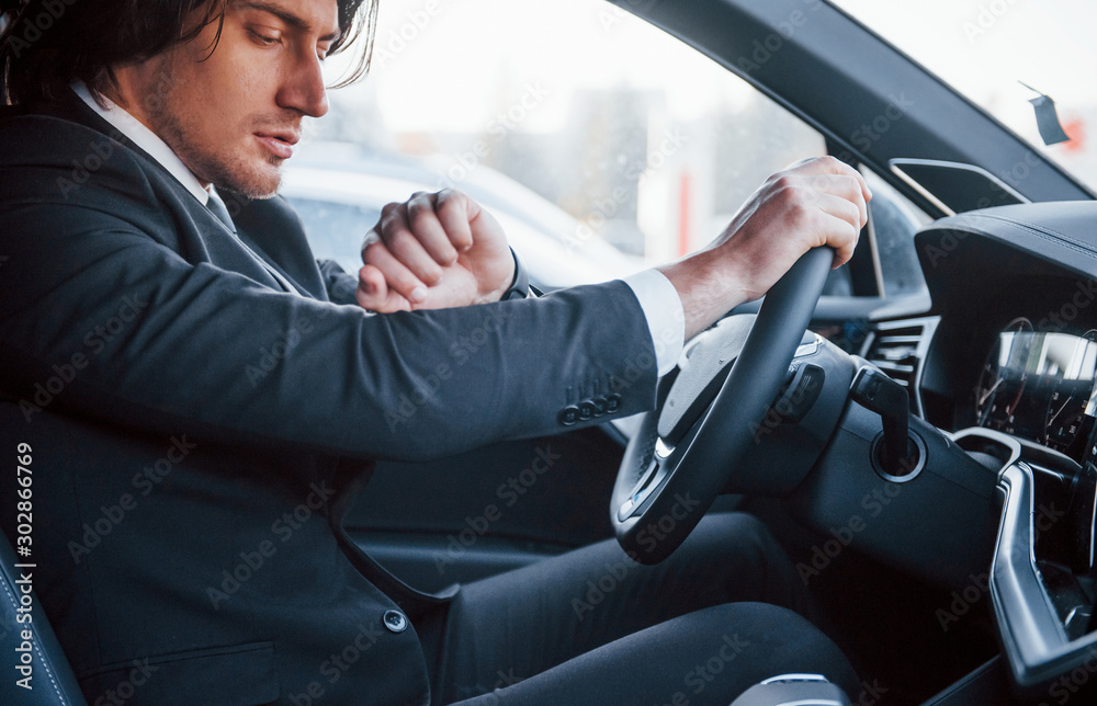 Young businessman in black suit and tie driving modern automobile