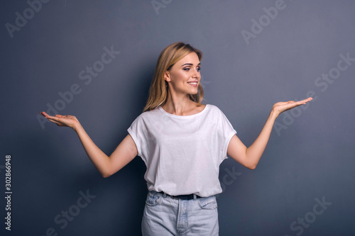 Caucasian woman in neutral casual outfit standing on a neutral grey background. Portrait with emotions: happiness, amazement, joy and satisfaction