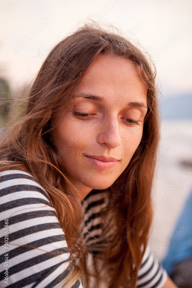 Portrait of a beautiful red-haired girl in T-shirt near the sea at the sunset. Pensive and happy girl. Relaxing near ocean. pretty girl Portrait of a beautiful red-haired girl in T-shirt near the sea at the sunset. Pensive and happy girl. Relaxing near ocean. pretty girl