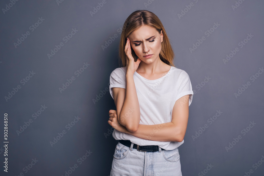 Caucasian woman in neutral casual outfit standing on a neutral grey background. Portrait with emotions: angry, pain, sickness and despair Caucasian woman in neutral casual outfit standing on a neutral grey background. Portrait with emotions: angry, pain, sickness and despair