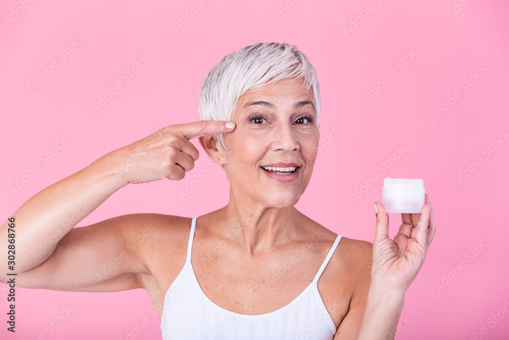 Smiling senior woman applying anti-aging lotion to remove dark circles under eyes. Mature woman using cosmetic cream to hide wrinkles. Lady using day moisturizer to counteract the aging of the skin. Smiling senior woman applying anti-aging lotion to remove dark circles under eyes. Mature woman using cosmetic cream to hide wrinkles. Lady using day moisturizer to counteract the aging of the skin.