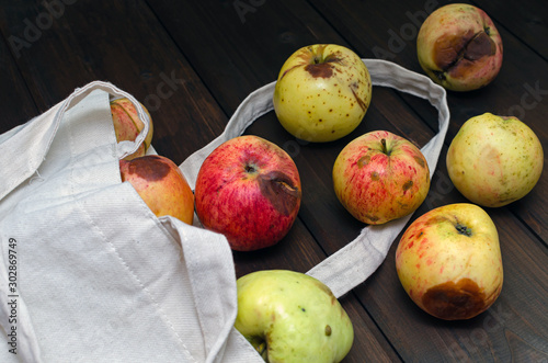 Zero waste concept. Red and yellow ugly apples in white textile bag on wooden background.