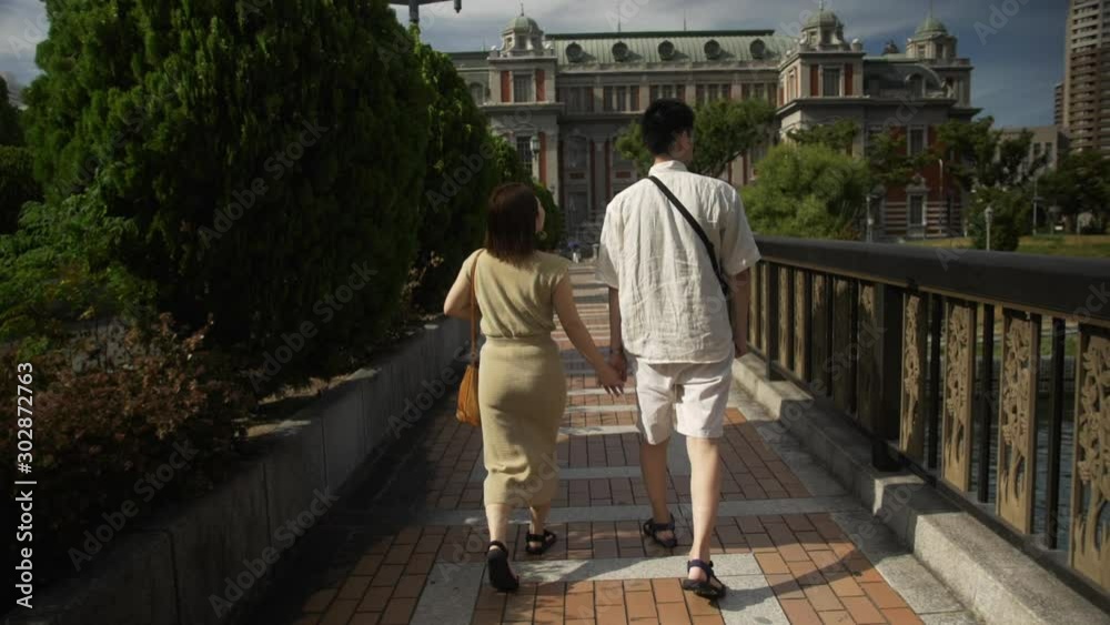 Couples holding their hands while they walk on a street during broad daytime with trees and plants around wearing casual clothes to feel relax as they do their vacation trip Couples holding their hands while they walk on a street during broad daytime with trees and plants around wearing casual clothes to feel relax as they do their vacation trip