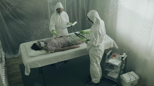 Two scientist attending to a woman with a virus lying on a stretcher in a field hospital photo