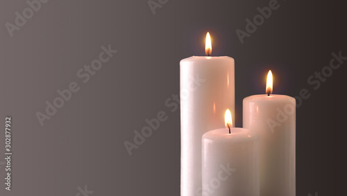 Three burning candles on gray degrading background photo