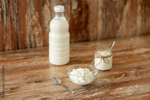 food and dairy products concept - bottle of milk, cottage cheese and homemade yogurt on wooden table