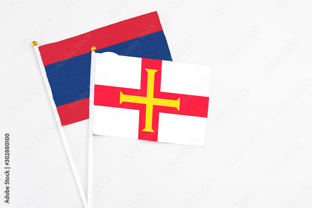 Guernsey and Laos stick flags on white background. High quality fabric, miniature national flag. Peaceful global concept.White floor for copy space.