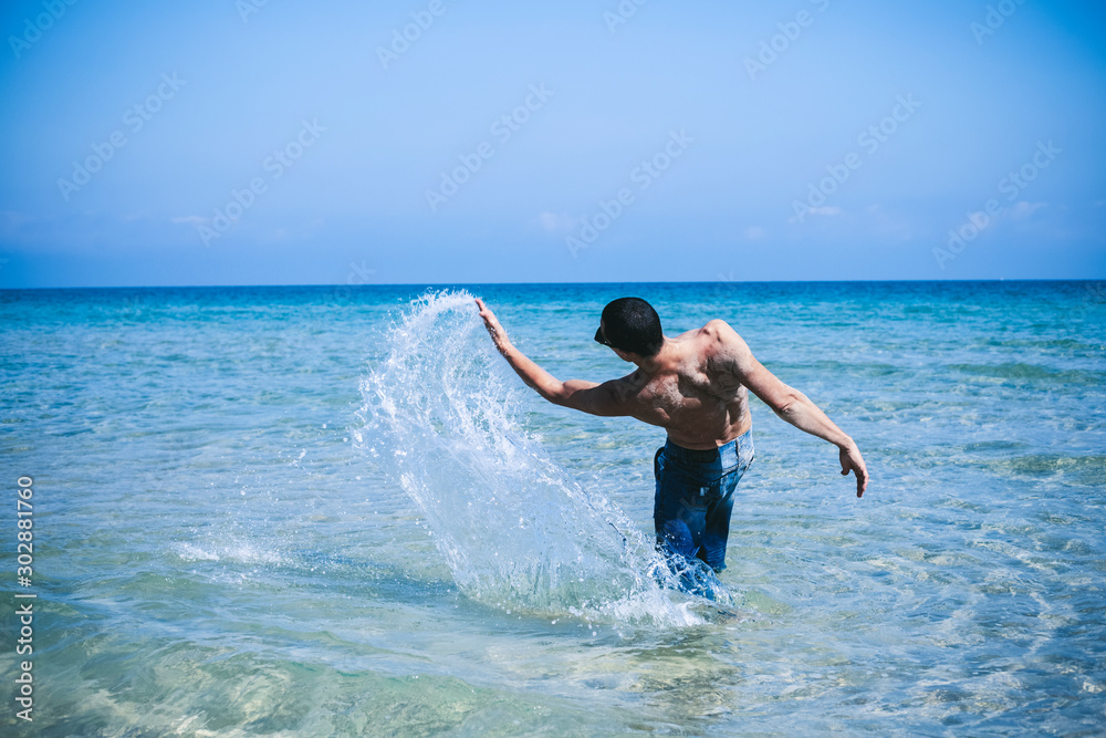 young muscular man posing and splashing around in the sea