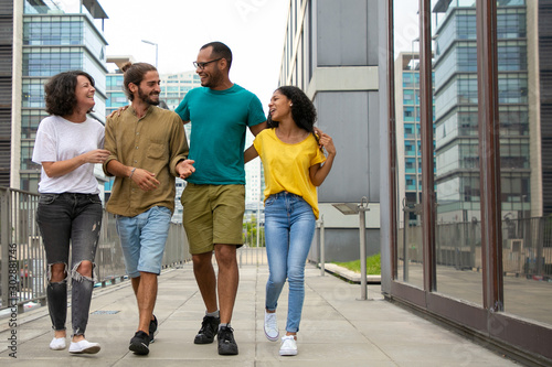 Happy young friends walking on street together. Cheerful young multiethnic men and women embracing and walking together outdoors. Friendship concept