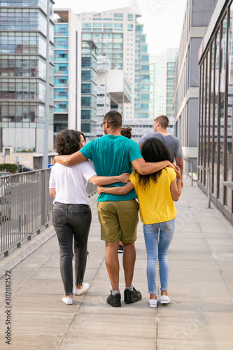 Back view of friends walking on street. Rear view of happy young multiethnic friends walking and talking outdoors. Friendship concept © Mangostar