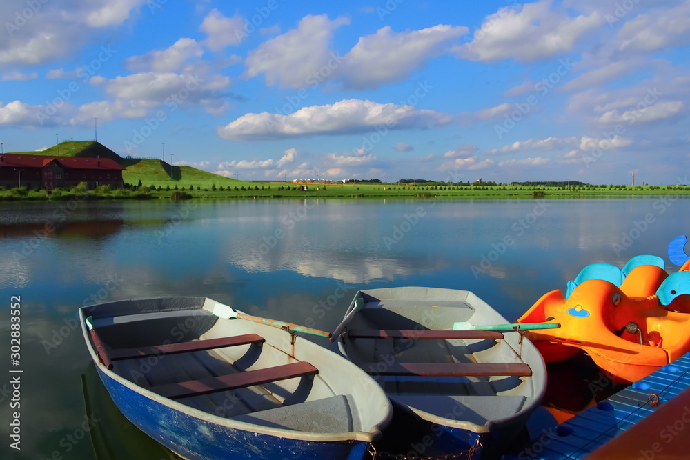 Two wooden rowing boats at the pier of the wonderful lake. white clouds are reflected in the calm blue surface of the water. summer sunny day. pastoral landscape. Two wooden rowing boats at the pier of the wonderful lake. white clouds are reflected in the calm blue surface of the water. summer sunny day. pastoral landscape.