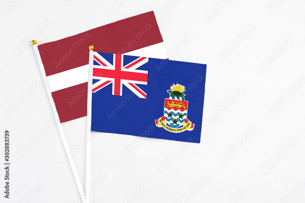 Fototapeta premium Cayman Islands and Latvia stick flags on white background. High quality fabric, miniature national flag. Peaceful global concept.White floor for copy space.