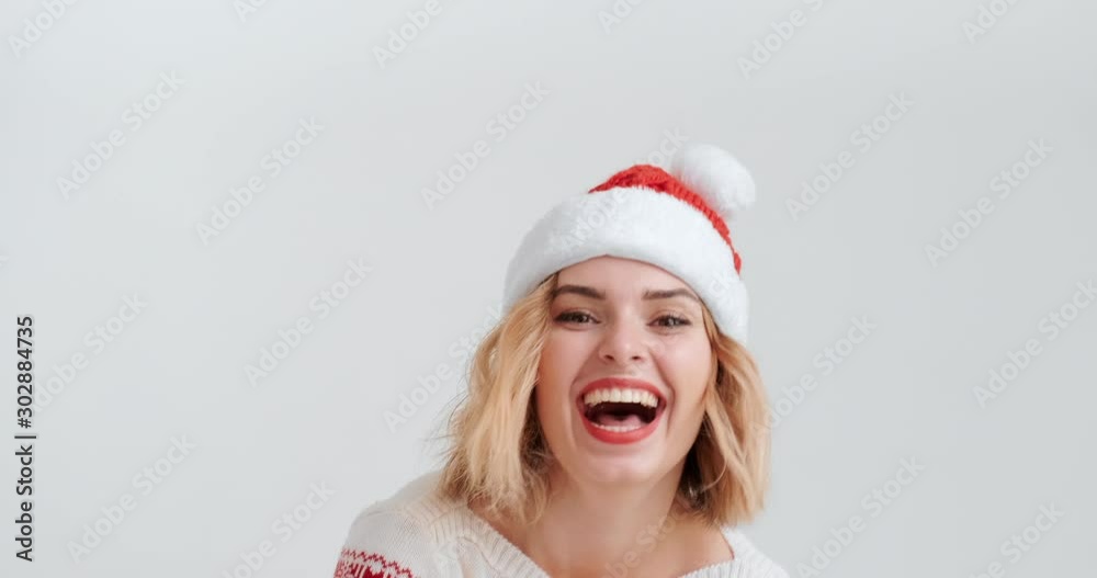 Young blond woman in red hat Christmas costume throws snowballs smiling while looking camera on white background. Santa Claus girl. Noel. Festive Сhristmas mood. Christmas preparation. Happy New Year Young blond woman in red hat Christmas costume throws snowballs smiling while looking camera on white background. Santa Claus girl. Noel. Festive Сhristmas mood. Christmas preparation. Happy New Year