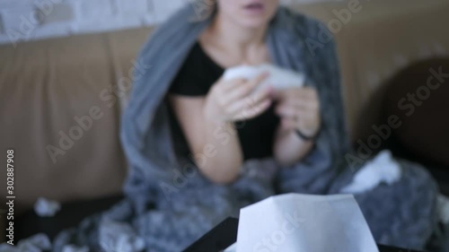 young caucasian woman sneezes takes handkerchief headache feel sick sitting at home on sofa virus illness cold ill temperature symptom health unhealthy young couch blanket infection pills medicine