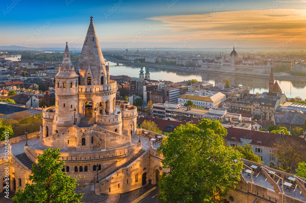 Naklejka premium Budapeszt, Węgry - piękny złoty wschód słońca latem z wieżą Baszty Rybackiej i zielonymi drzewami. Parlament Węgier i Dunaju w tle. Niebieskie niebo.