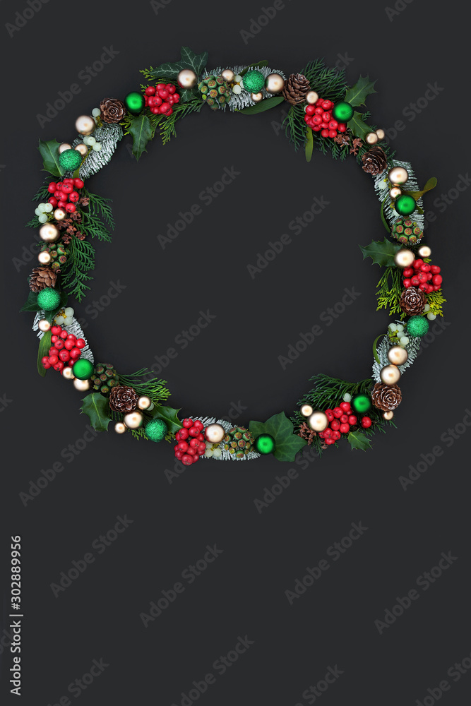 Christmas wreath with winter flora of holly, ivy, mistletoe, cedar and pine cones with gold and green bauble decorations on dark grey background with copy space. 