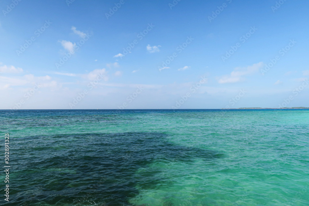 The sea has many colors as blue, dark green, light green but low waves. intersection against the horizon with a little cloudy, sunny, not appearing other objects. Taken at Maafushi Island, Maldives