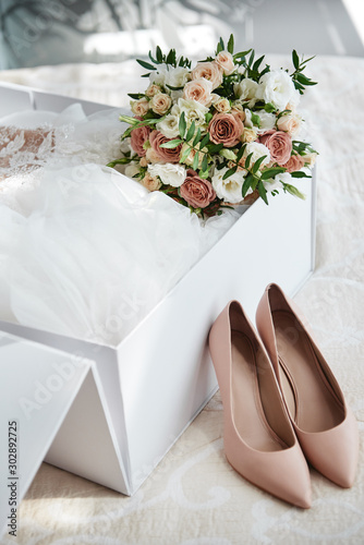 Photo Luxury wedding dress in white box, beige women's shoes and bridal bouquet on bed, copy space