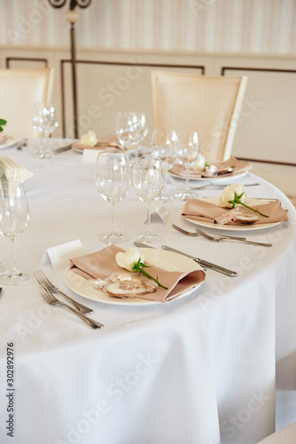 Table setting with blank guest card, white plate with beige serviette, rose, heart and cutlery on table, copy space. Place setting at wedding reception. Table served for wedding banquet in restaurant