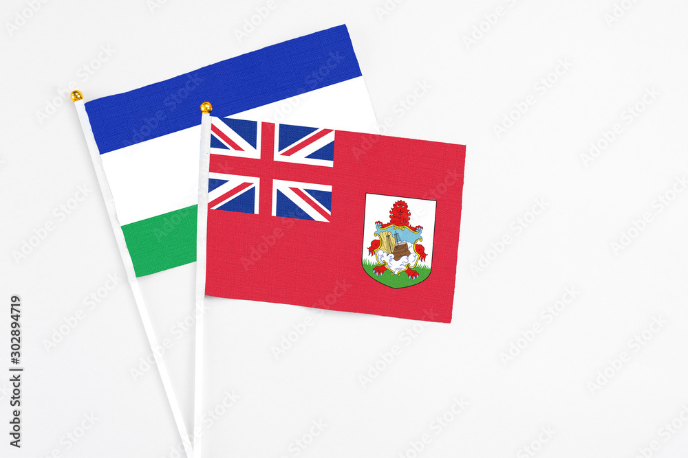 Fototapeta premium Bermuda and Lesotho stick flags on white background. High quality fabric, miniature national flag. Peaceful global concept.White floor for copy space.