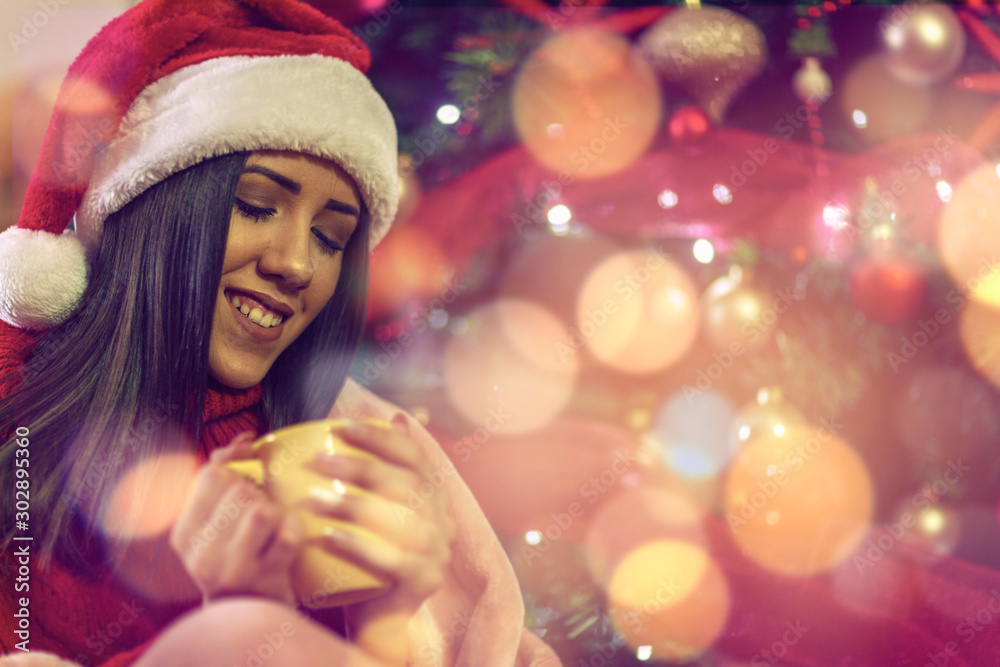 Smiling girl in Santa hat drinking tea over christmas treeat home
