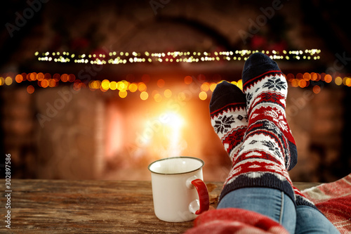 Blurred background of chrsitmas fireplace.Orange color of warm light of fire.Woman legs with socks and jeans.Copy space.Free place for your decoration.Cold winter december night.Christmas Eve party.