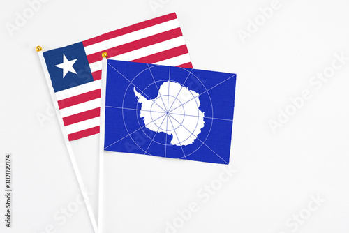 Antarctica and Liberia stick flags on white background. High quality fabric, miniature national flag. Peaceful global concept.White floor for copy space.