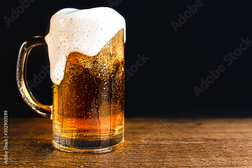 Cold beer with foam in a mug, on a wooden table and a dark background with bl...