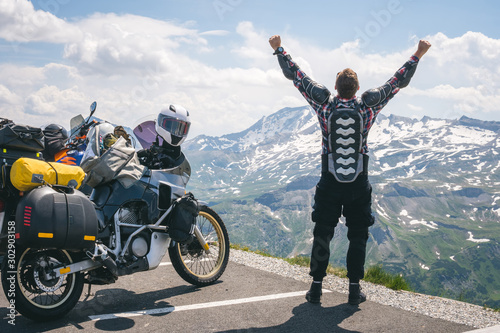A motorcycle traveler is happy arrived at his destination. Conquering the top of the mountain, Grossglockner pass, biker dressed in a protective jacket armor of the body of a turtle. Austria