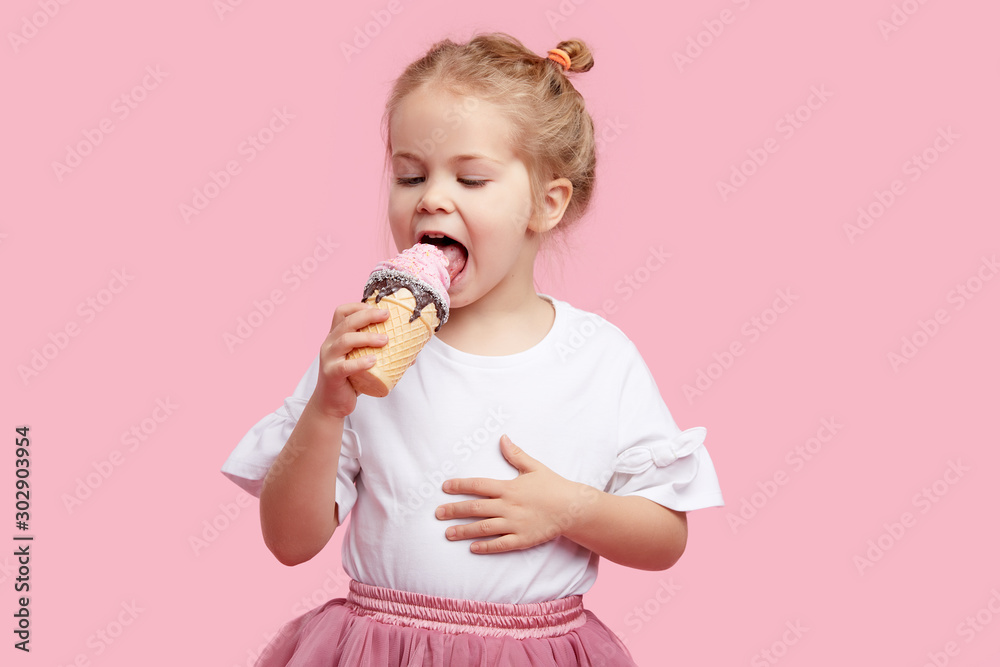 Cute child girl with pleasure eats tasty ice-cream on a pink studio ...