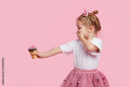 Cuadro en lienzo Cute child girl holds ice cream on his outstretched arm and covers his mouth with his hand